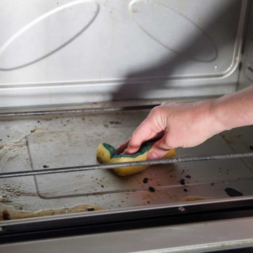 Cleaning the oven from burnt drops with a sponge, dirty oven